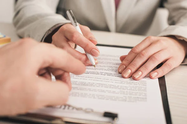 Foyer sélectif de l'agent immobilier pointant avec le doigt au presse-papiers avec lettrage près du client — Photo de stock