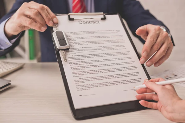 Vista recortada del agente sujetando portapapeles con letras de contrato y llave del coche cerca de la mujer — Stock Photo