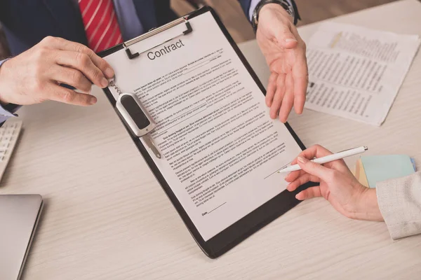 Ausgeschnittene Ansicht des Agenten, der mit der Hand auf Klemmbrett mit Vertragsbeschriftung und Autoschlüssel in Kundennähe zeigt — Stockfoto