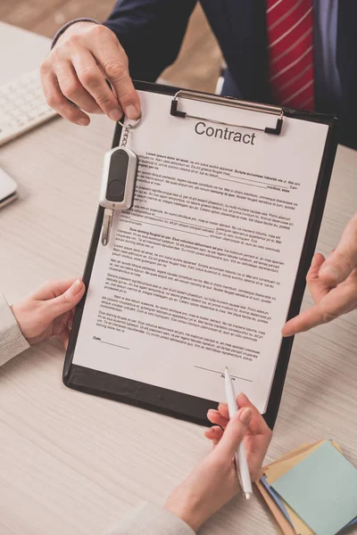 Cropped view of agent pointing with finger at clipboard with contract lettering and car key near client — Stock Photo