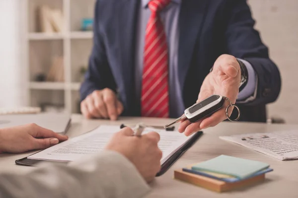 Selective focus of agent holding car key near client signing contract — Stock Photo