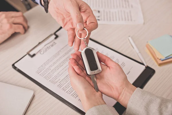 Cropped view of agent giving car key to client near clipboard with contract — Stock Photo