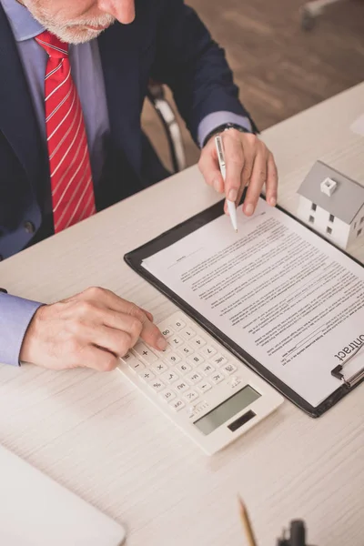 Cropped view of bearded broker using calculator and holding pen near clipboard — Stock Photo