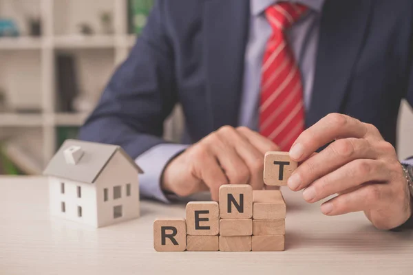 Vue recadrée de l'agent tenant cube en bois avec lettrage près du modèle de maison en carton — Photo de stock