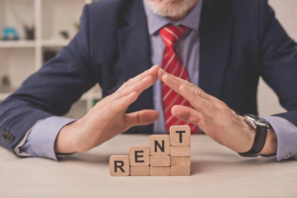 Cropped view of agent putting hands above wooden cubes with rent lettering — Stock Photo