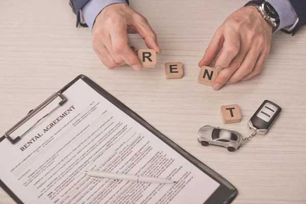 Cropped view of agent holding wooden cubes with rent lettering near clipboard and car key — Stock Photo
