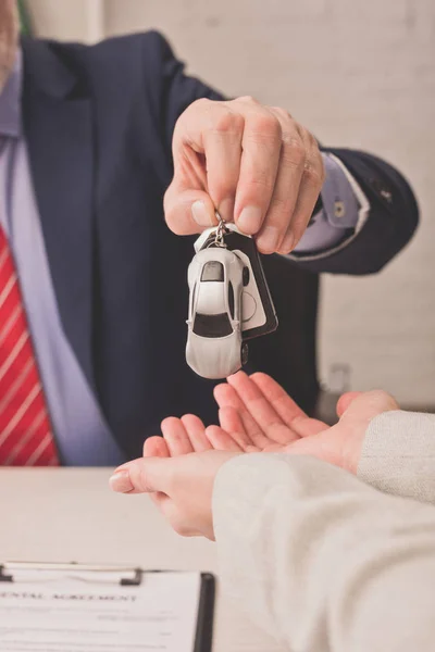 Vista cortada do agente dando a chave do carro ao cliente com as mãos de chávena — Fotografia de Stock