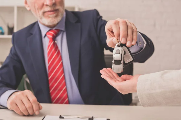 Vista cortada do agente barbudo dando a chave do carro ao cliente com a mão de copo — Fotografia de Stock