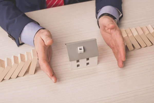 Top view of agent putting hands on desk between wooden cubes and carton house model — Stock Photo