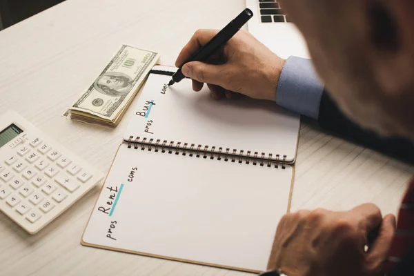 Selective focus of agent writing in notebook with rent and buy lettering near money and calculator — Stock Photo