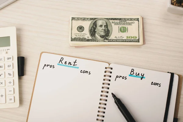 Vista superior de notas de dólar perto notebook com alugar e comprar letras, caneta marcador e calculadora — Fotografia de Stock