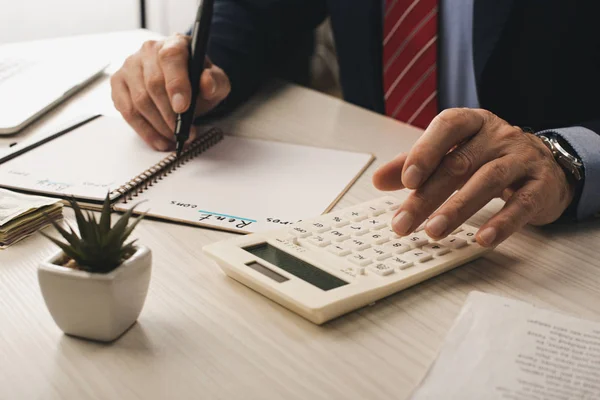 Cropped view of agent writing in notebook with rent and buy lettering near plant and calculator — Stock Photo