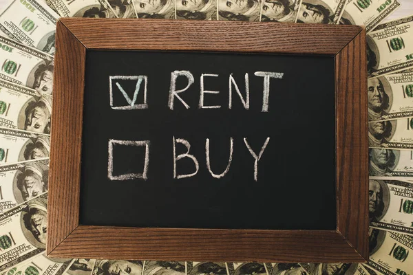 Top view of chalkboard with rent and buy lettering near dollar banknotes — Stock Photo