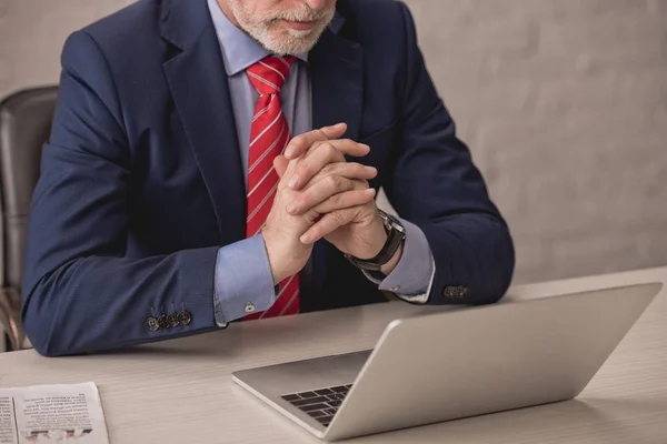 Обрезанный вид бизнесмена с сжатыми руками возле ноутбука — стоковое фото