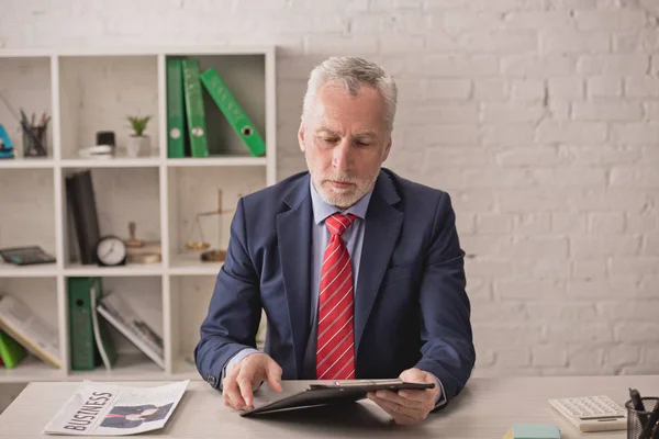 Bearded realtor looking at clipboard near business newspaper on desk — Stock Photo