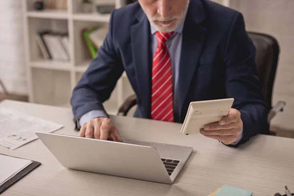 Vista recortada del hombre de negocios utilizando el ordenador portátil y la calculadora de retención - foto de stock