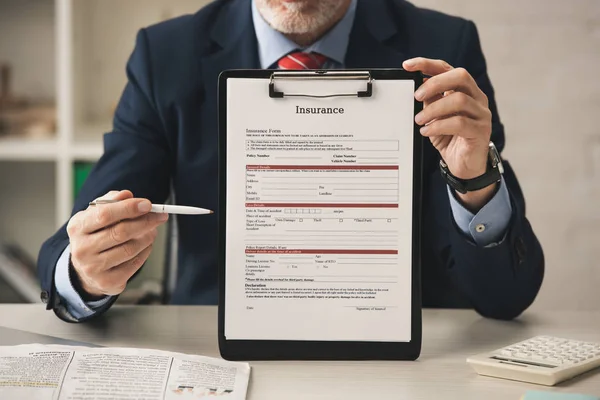 Ausgeschnittene Ansicht eines bärtigen Agenten, der Stift in der Nähe von Klemmbrett mit Versicherungsbuchstaben und Taschenrechner hält — Stockfoto