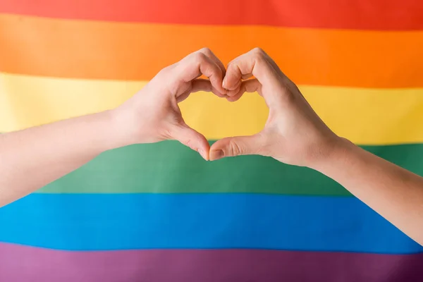 Обрізаний вид жінки, що показує серце руками біля прапора ЛГБТ, концепція прав людини — стокове фото
