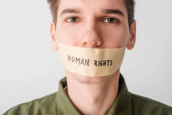 Hombre con cinta adhesiva en la boca con letras de derechos humanos aisladas en blanco - foto de stock