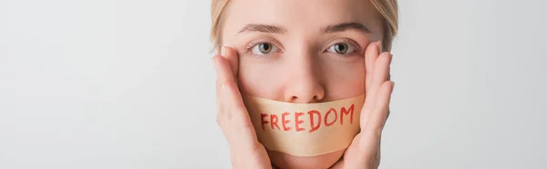 Plano panorámico de la mujer con cinta adhesiva en la boca con letras de libertad aisladas en blanco, concepto de derechos humanos - foto de stock