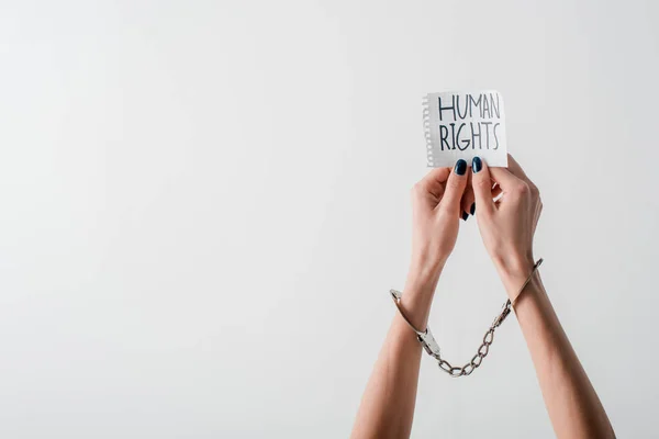 Vista recortada de la mujer con esposas en las manos sosteniendo papel con letras de derechos humanos aisladas en blanco - foto de stock