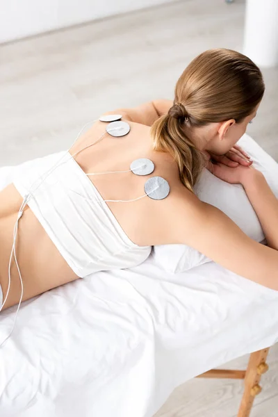Visão traseira da mulher com eletrodos nas costas no sofá de massagem durante o tratamento do eletrodo — Fotografia de Stock