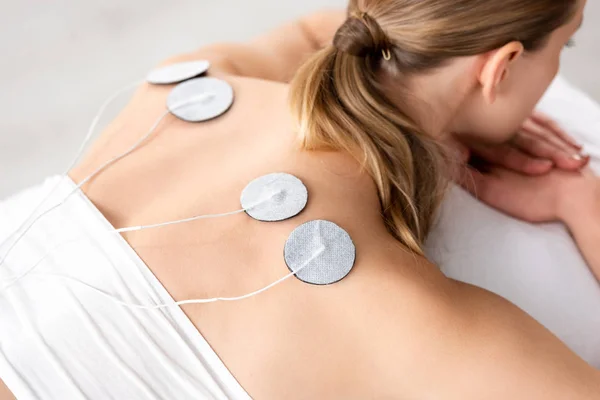 High angle view of young woman with electrodes on back during electrode treatment on grey background — Stock Photo