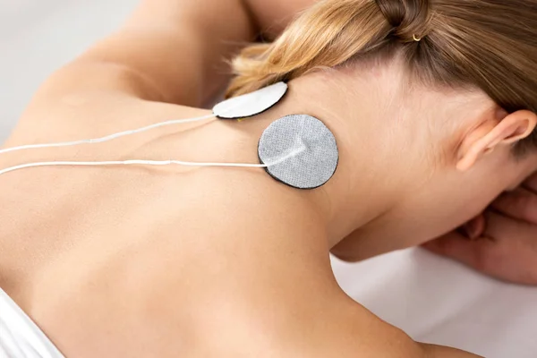 Vista posteriore di giovane donna con elettrodi di elettrostimolazione sul collo sul divano massaggio isolato su grigio — Foto stock