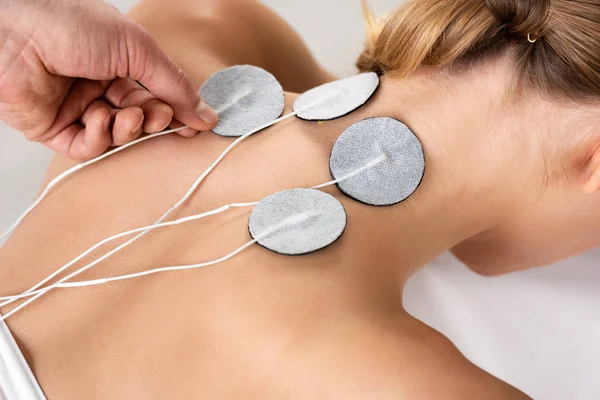 Vista recortada de los electrodos de fijación del terapeuta en el cuello del paciente durante el tratamiento con electrodos aislados en gris - foto de stock