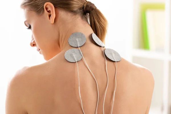Rückenansicht der schönen Frau mit Elektroden am Hals während der Elektrotherapie in der Klinik — Stockfoto