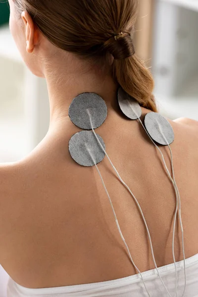 Vista posterior de los electrodos del cuello de la mujer joven durante el tratamiento de electrodos en la clínica - foto de stock