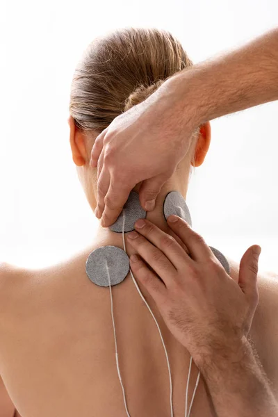 Terapeuta que sostiene electrodos de estimulación en el cuello del paciente durante el tratamiento con electrodos aislados en blanco - foto de stock