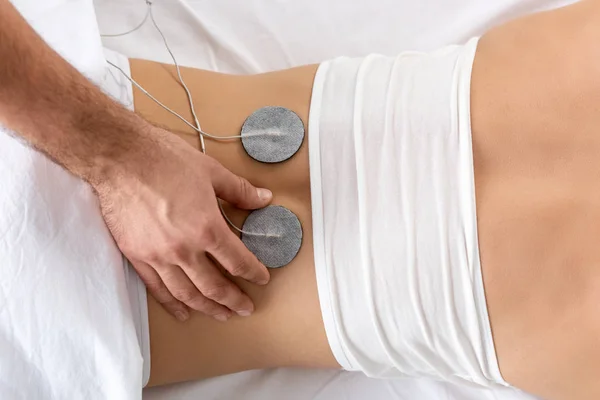 Vista superior del electrodo de ajuste del terapeuta en la espalda del paciente durante la electroterapia en el sofá de masaje - foto de stock