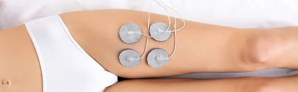 Top view of woman in panties lying on massage couch during electrode treatment of leg, panoramic shot — Stock Photo