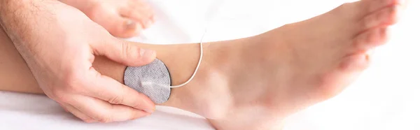 Cropped view of therapist setting electrode on leg of patient on massage couch, panoramic shot — Stock Photo