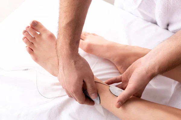 Cropped view of therapist fastening stimulation electrodes on patient leg isolated on grey — Stock Photo