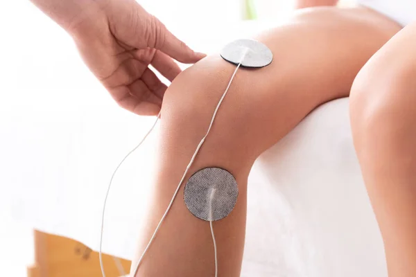 Vista recortada de electrodos de ajuste del terapeuta en la rodilla del paciente en el sofá de masaje sobre fondo blanco - foto de stock