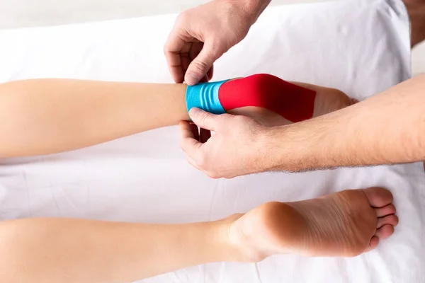 Top view of doctor applying kinesiology tapes on feet of patient on massage couch — Stock Photo