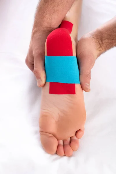 Cropped view of dactor applying kinesiology tapes on heel of patient on massage couch — Stock Photo