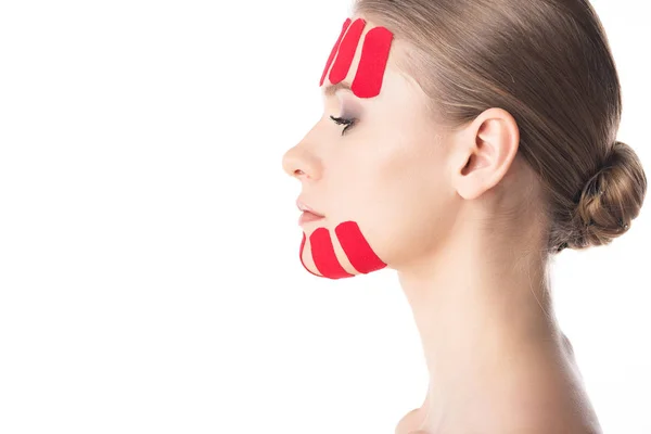 Vista lateral de hermosa chica con cintas de kinesiología en la cara aislada en blanco - foto de stock