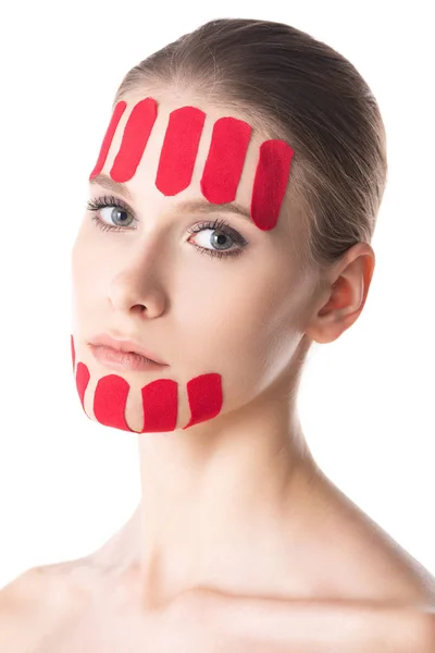 Attraktive Frau mit Kinesiologie-Klebebändern im Gesicht, die auf weiß isoliert in die Kamera blickt — Stockfoto