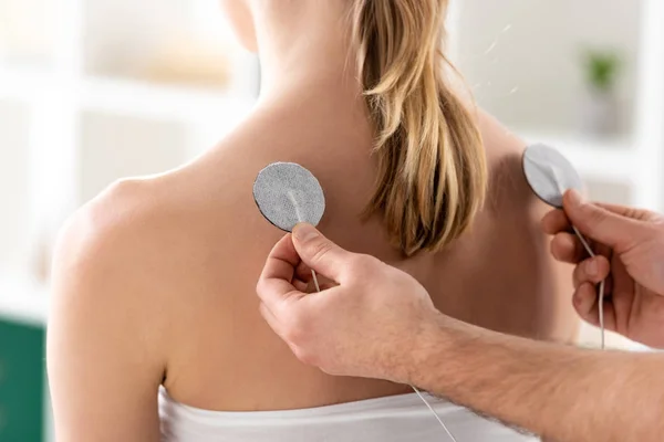 Cropped view of doctor fastening electrodes of patient back during electrotherapy in clinic — Stock Photo
