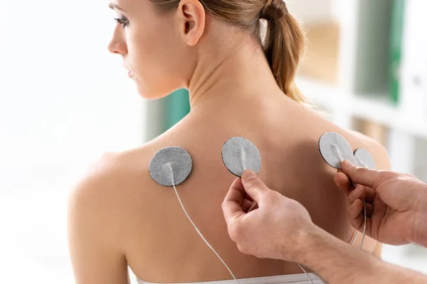 Électrodes de réglage thérapeute sur le dos de belle femme pendant le traitement des électrodes — Photo de stock