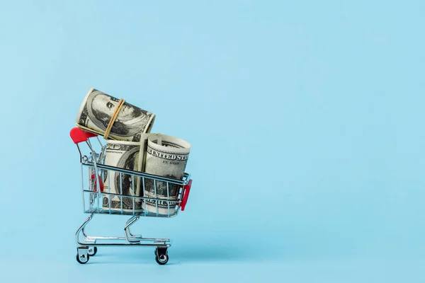 Toy shopping cart with dollar banknotes on blue, leasing concept — Stock Photo
