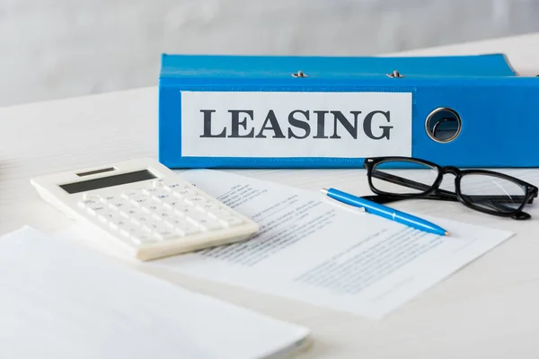 Selective focus of folder with leasing lettering near calculator, pen and glasses on desk — Stock Photo