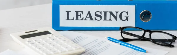 Panoramic shot of folder with leasing lettering near calculator, pen and glasses on desk — Stock Photo