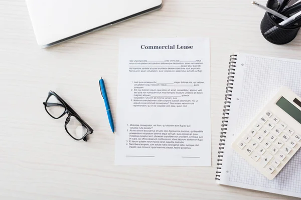 Vista superior del documento con letras de arrendamiento comercial, pluma, calculadora, computadora portátil y gafas cerca del portátil en el escritorio - foto de stock