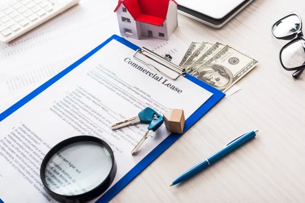 Dokument mit gewerblichem Leasingaufdruck auf Klemmbrett in der Nähe von Schlüsseln, Geld, Hausmodell, Stift, Lupe und Brille — Stockfoto