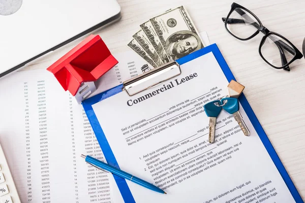 Vue du haut du document avec lettrage de bail commercial sur presse-papiers près des clés, de l'argent, du modèle de maison, du stylo et des lunettes — Photo de stock