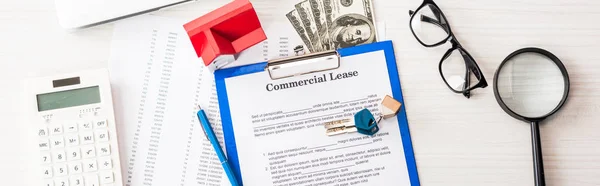 Panoramic shot of document with commercial lease lettering on clipboard near keys, house model, pen, calculator and glasses — Stock Photo